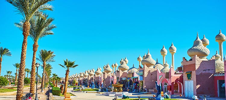 Palm trees and whimsical beach-style buildings line a sunlit boulevard in Hurghada, Egypt, the backdrop to the "Fantasia 1,001" show.